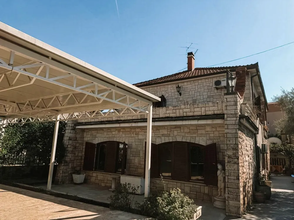 Kamena kuća sa drvenim škurama i bijelom čeličnom nadstrešnicom, prije radova.